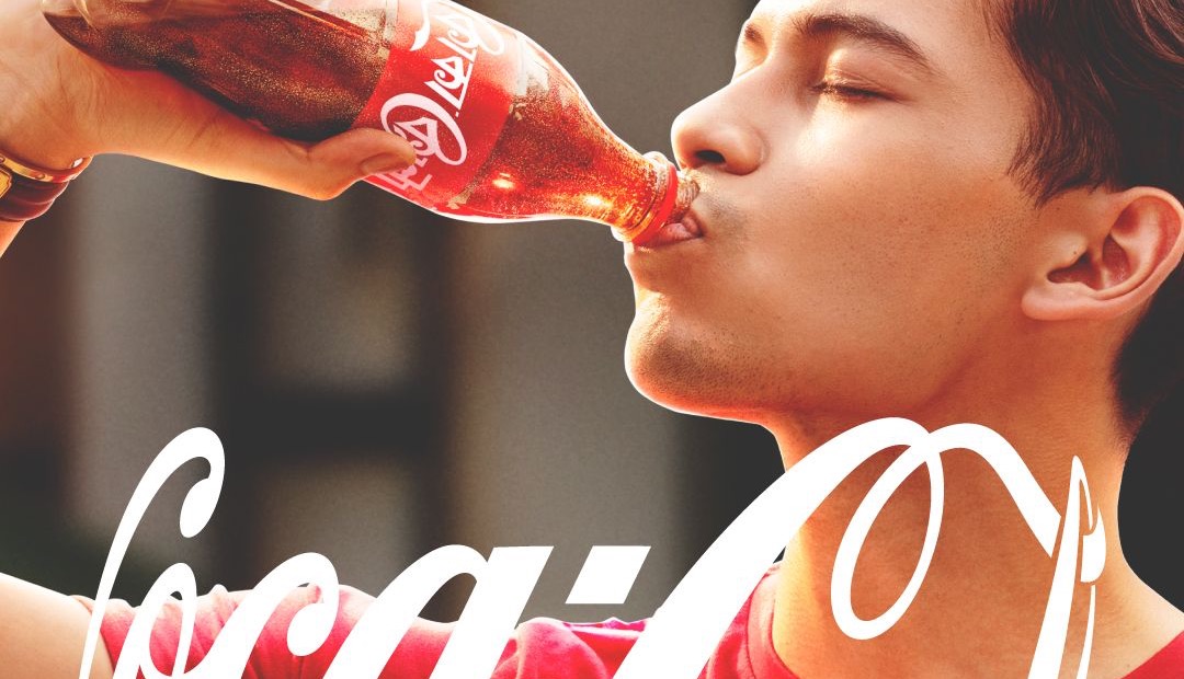 Young man drinking from a Coke bottle, eyes closed, logo overlaid