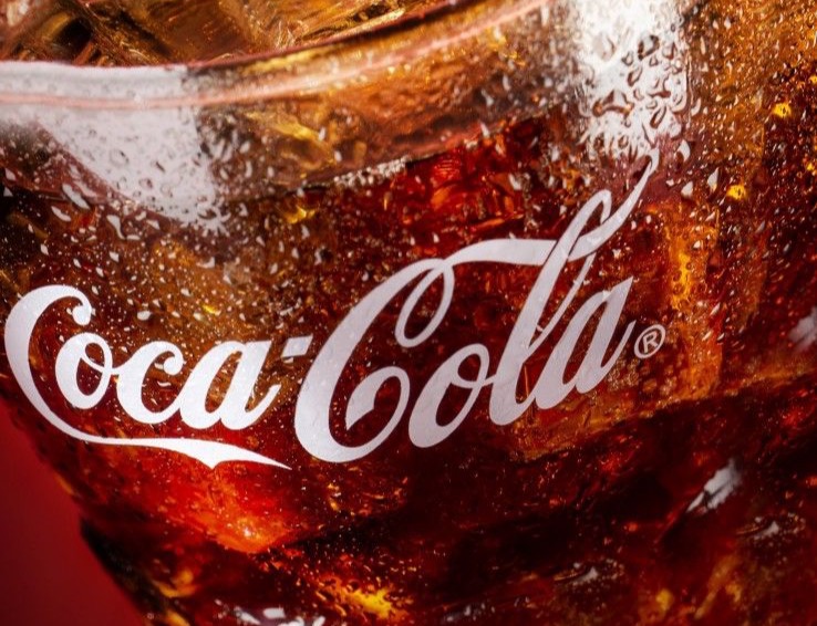 Ice-filled glass with amber Coke and a sweating logo, close up