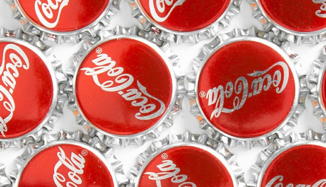 Flat-lay pattern of Coke bottle caps, top down on white
